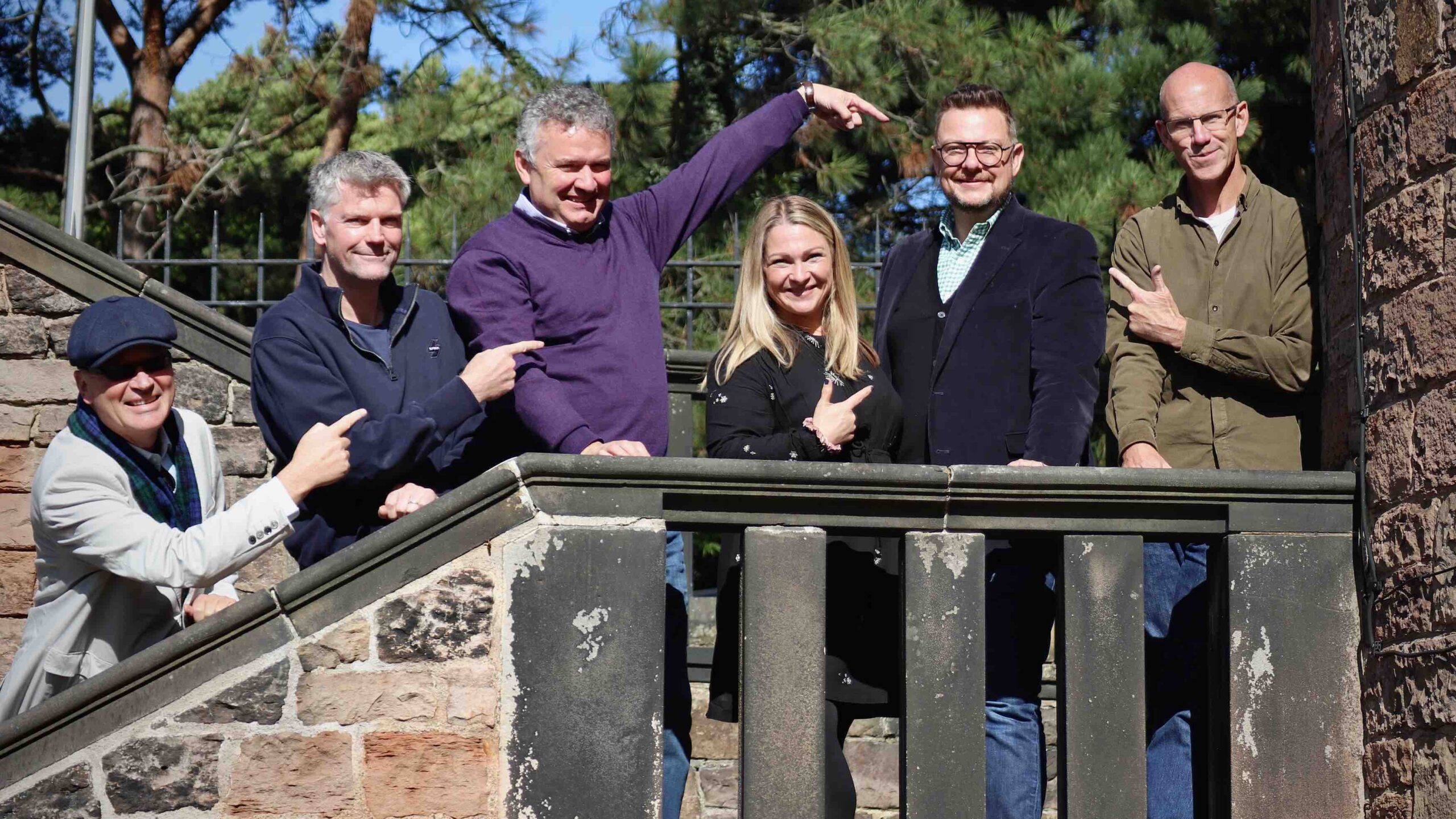 Group of people on a stair case outside, pointing to one man