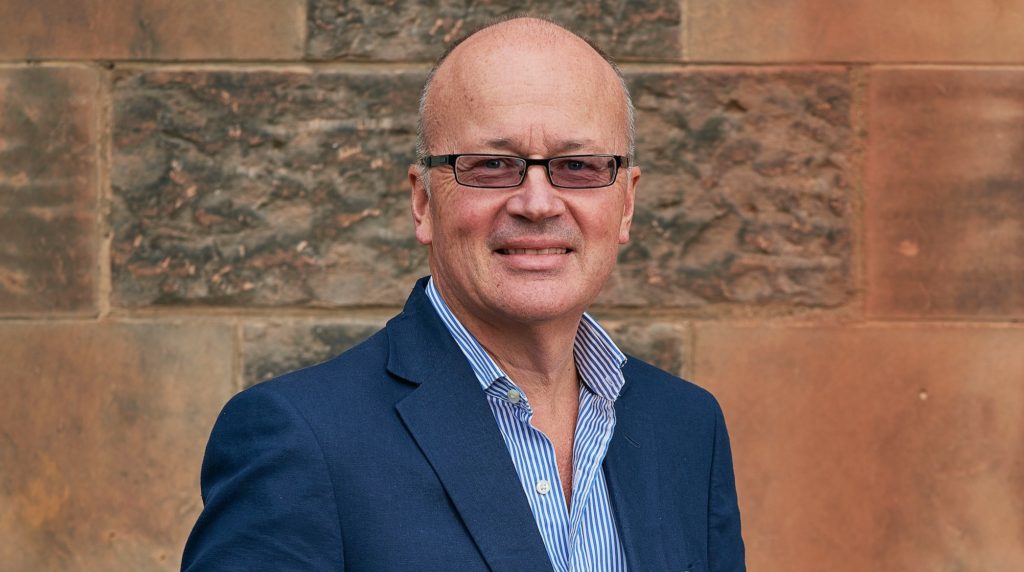 Man with glasses, wearing a blue suit and blue shirt looking to camera Ian McAteer