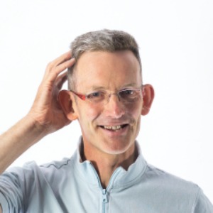 Image of man with glasses looking to camera with one hand touching the top of his head