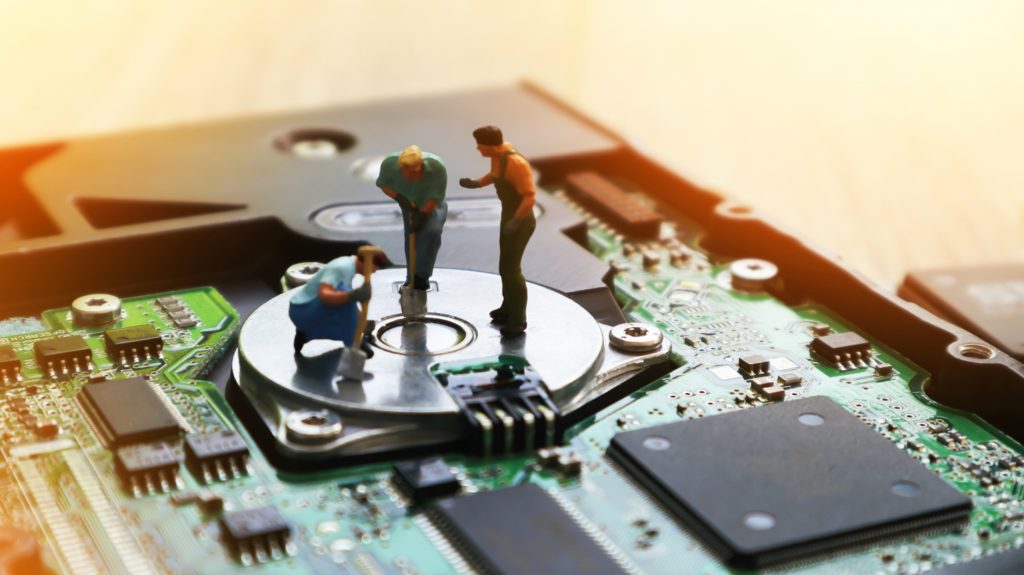 three miniatures of people on top of a computer hard drive looking down