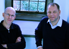 Two men looking to camera in front of window