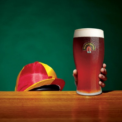 Small Jockey reaching up behind a bar for a pint of John Smith's, only seeing the red and yellow striped hat of the Jockey