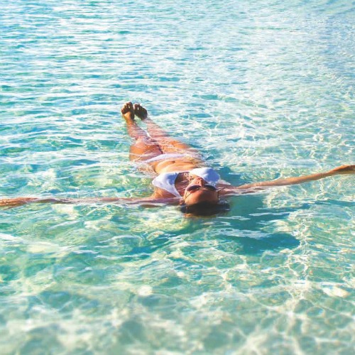 Woman laying back in clear blue water in a white bikini