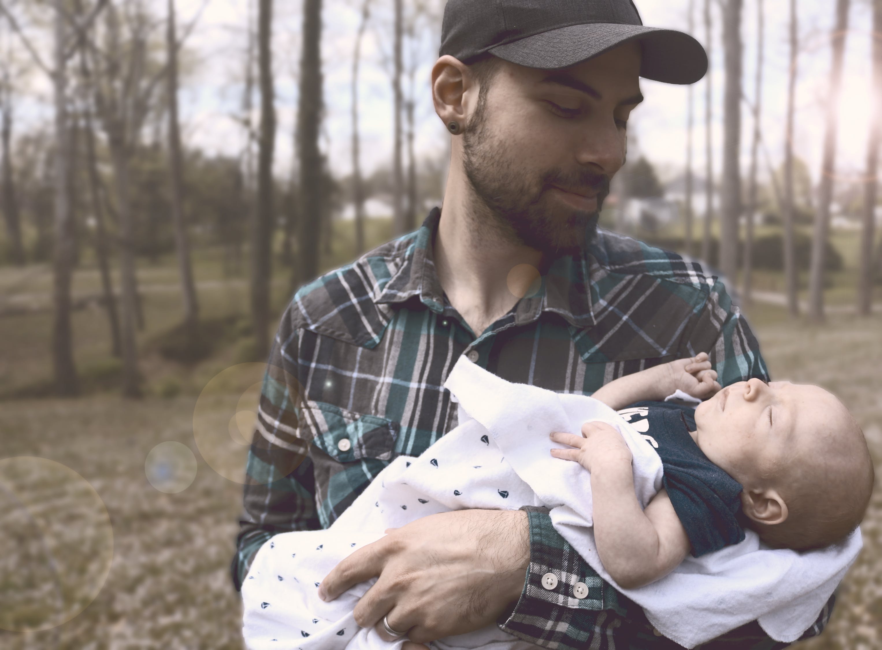 Man with baseball cap on holding baby in his arms