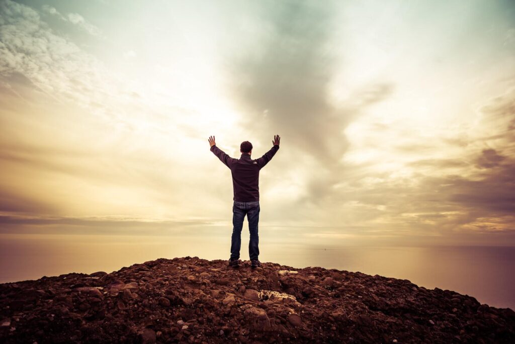 Man standing with arms raised to the sky on the rock edge overlooking the ocean