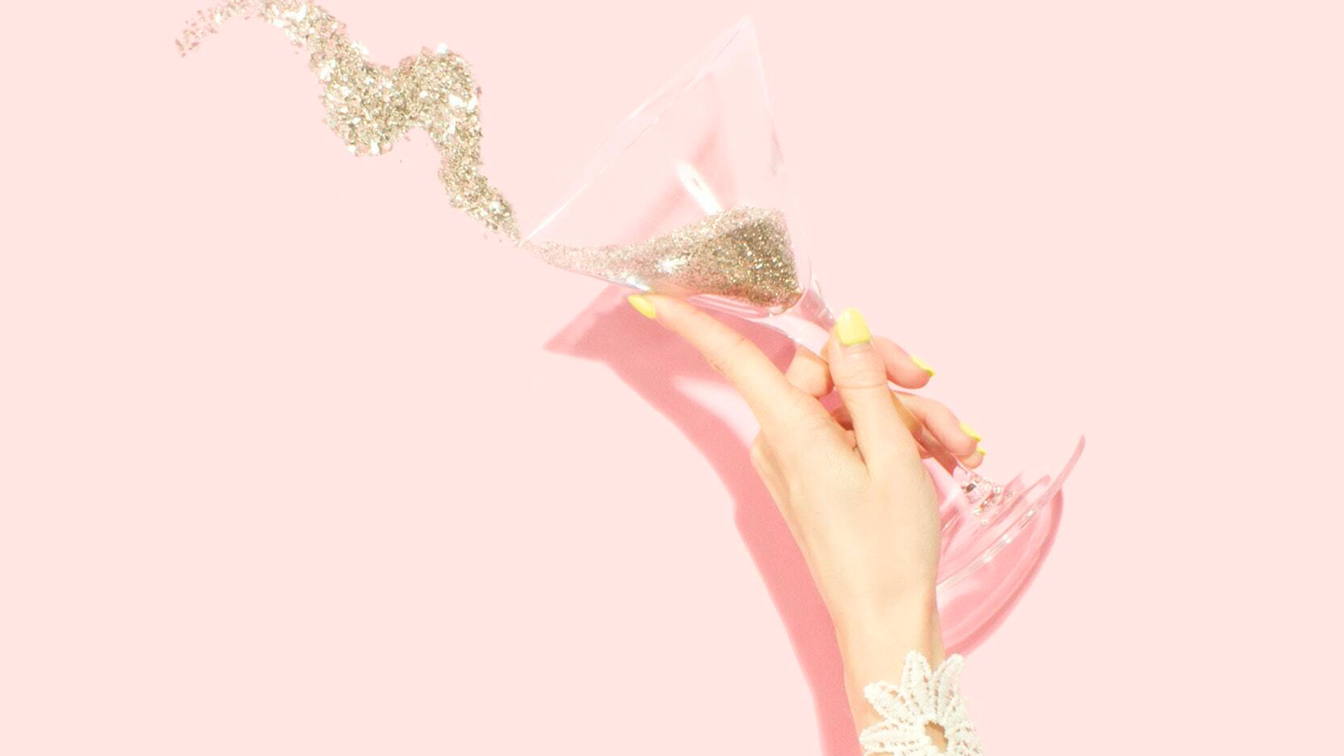 Woman's hand tossing cocktail glass containing glitter