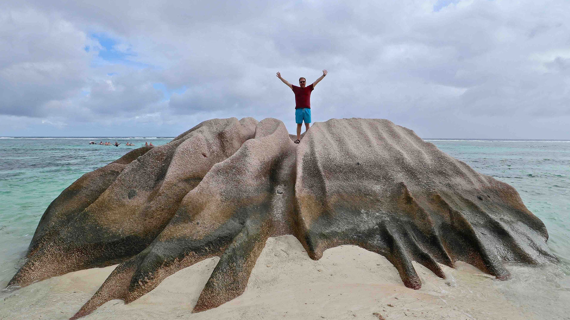 Man with outstretched arms on rock in front of beach