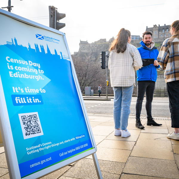 Group on people on the street in the background speaking in front of a sign