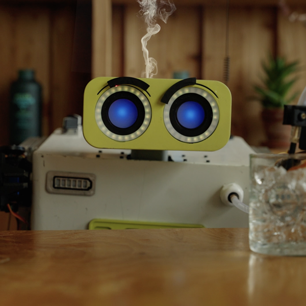 small robot at desk with a glass in front of it trying to plug into the glass of ice