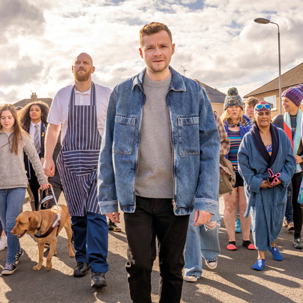 Man walking smiling, with a large group of random people following him on the street