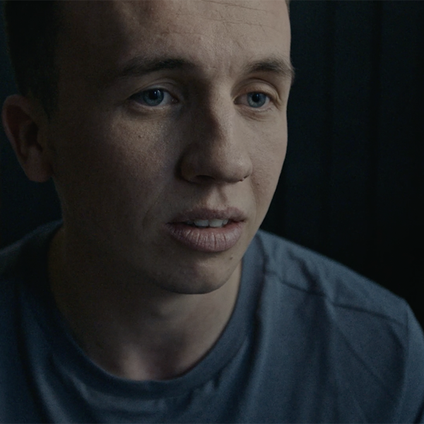 Man looking to camera sat down in a grey top looking sad