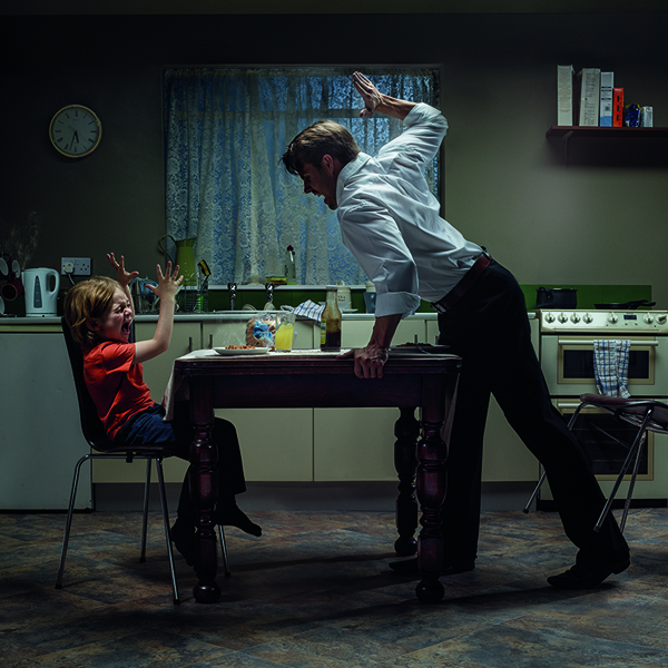 Man at table about to slap a small child sat opposite at the table