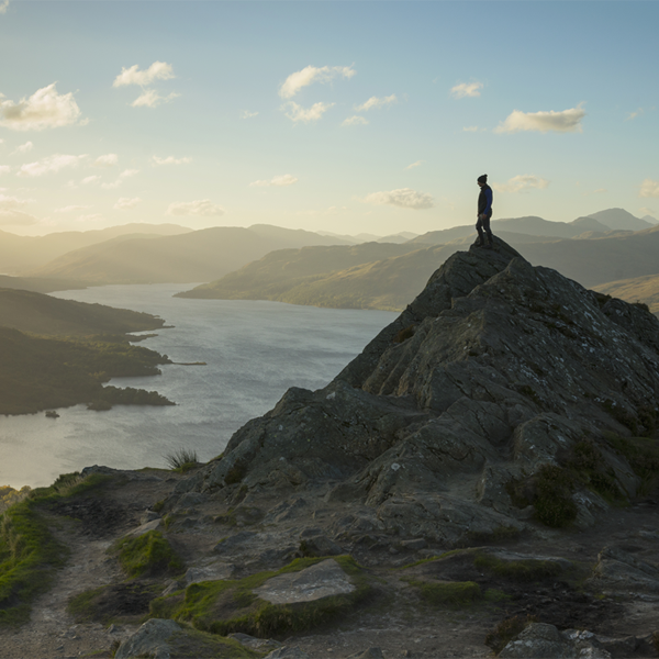 Man on hill top overlooking loch and valley