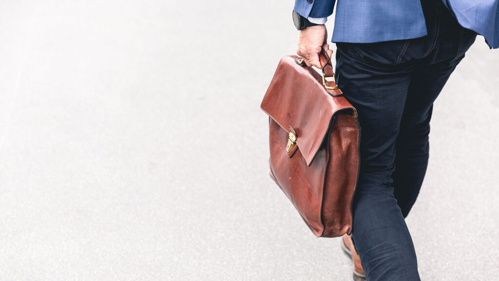 Man waling on the street holding a brown briefcase