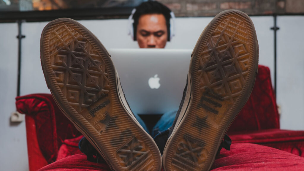 Man laying down working on a laptop and with headphones on.