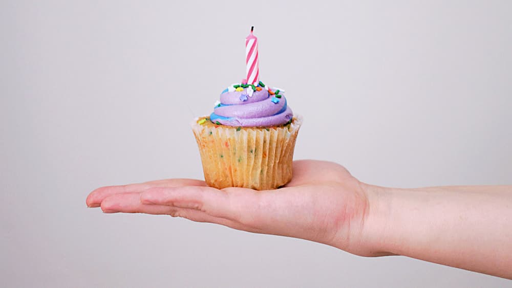 hand holding a cupcake with a candle in it