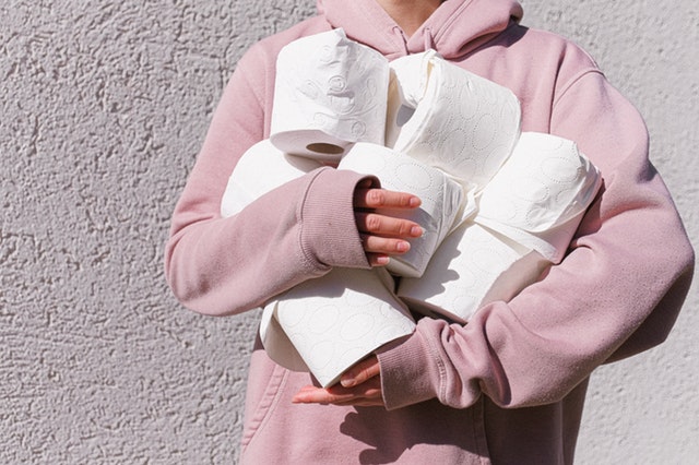 woman in pink top holding toilet paper rolls