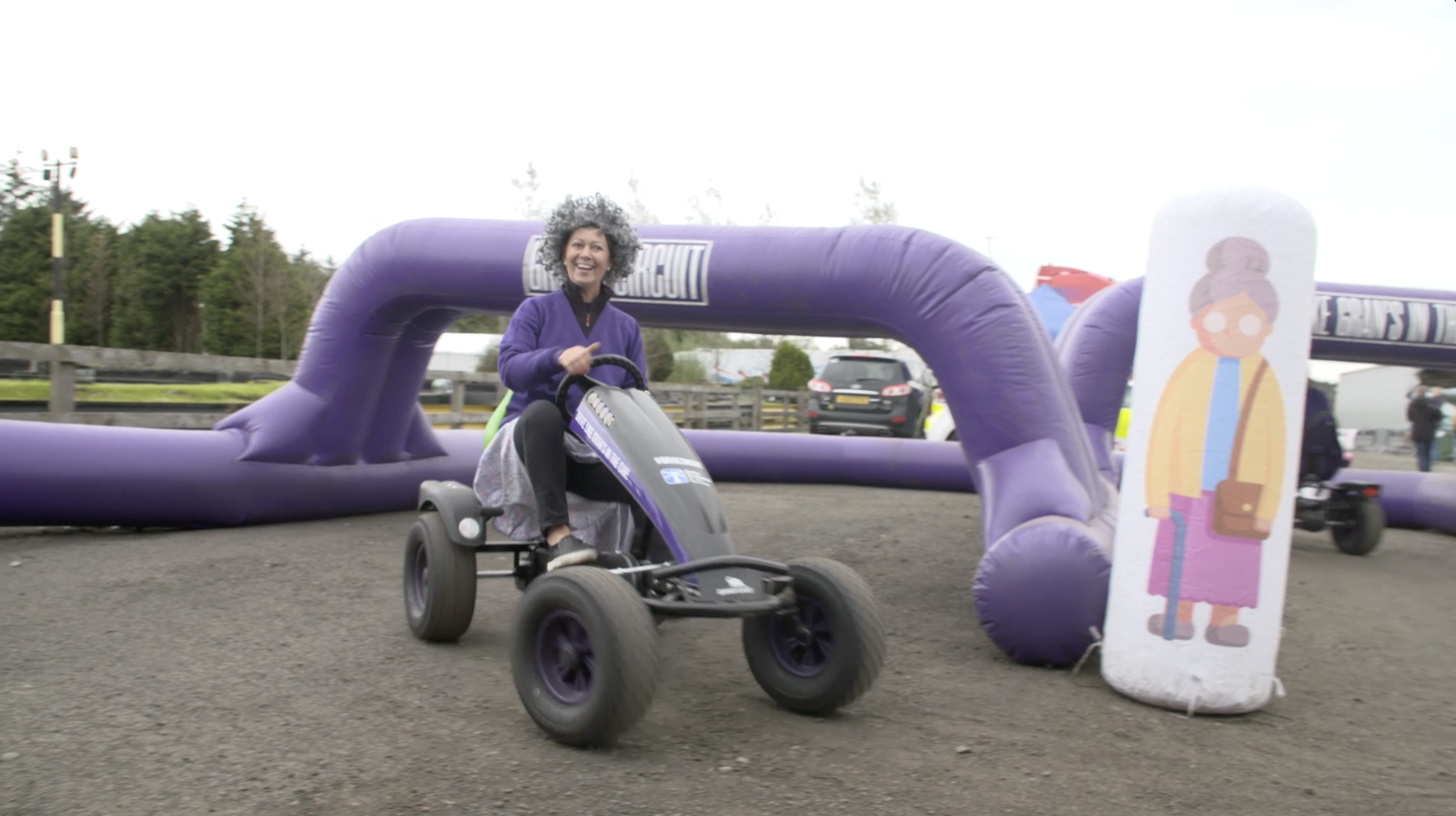 Woman dressed as an old lady driving a go-kart