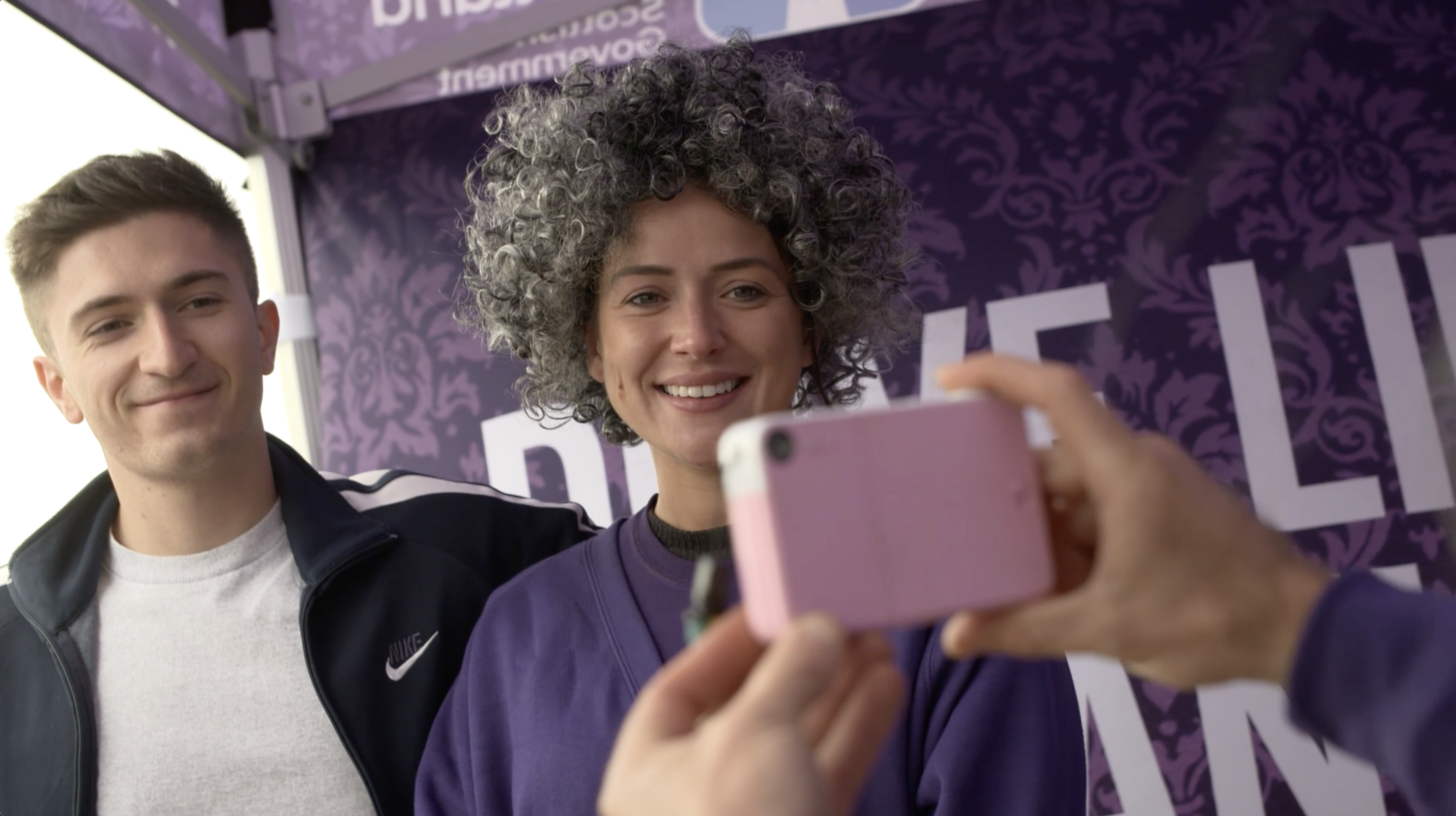 Young woman dresses like an old lady, having photo taken with young man