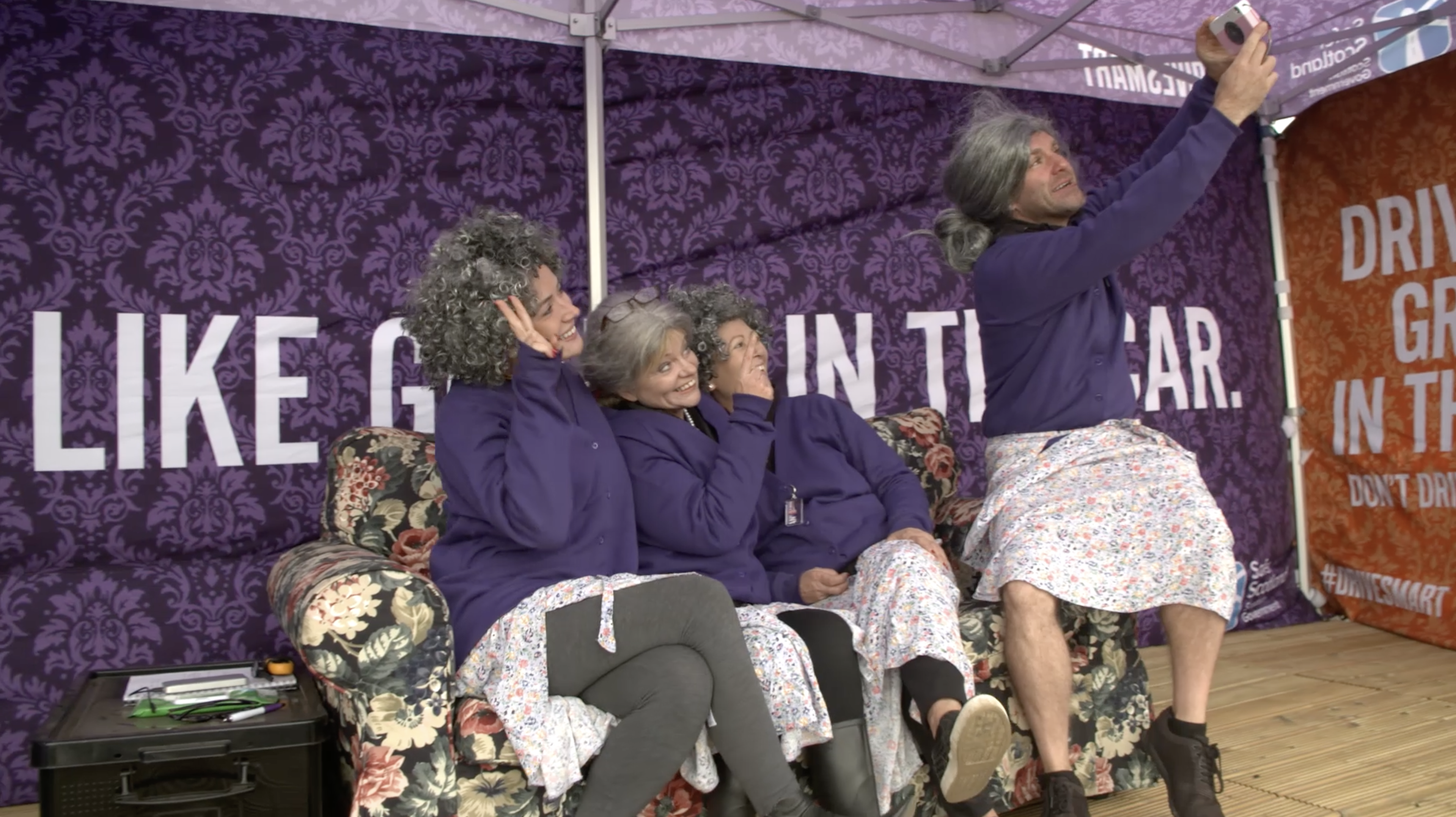 Group of men and women sat on couch dressed as old ladies taking a selfie