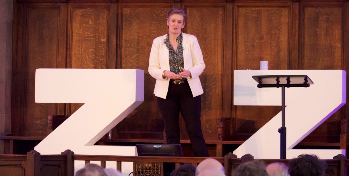 Woman on stage speaking to group of people