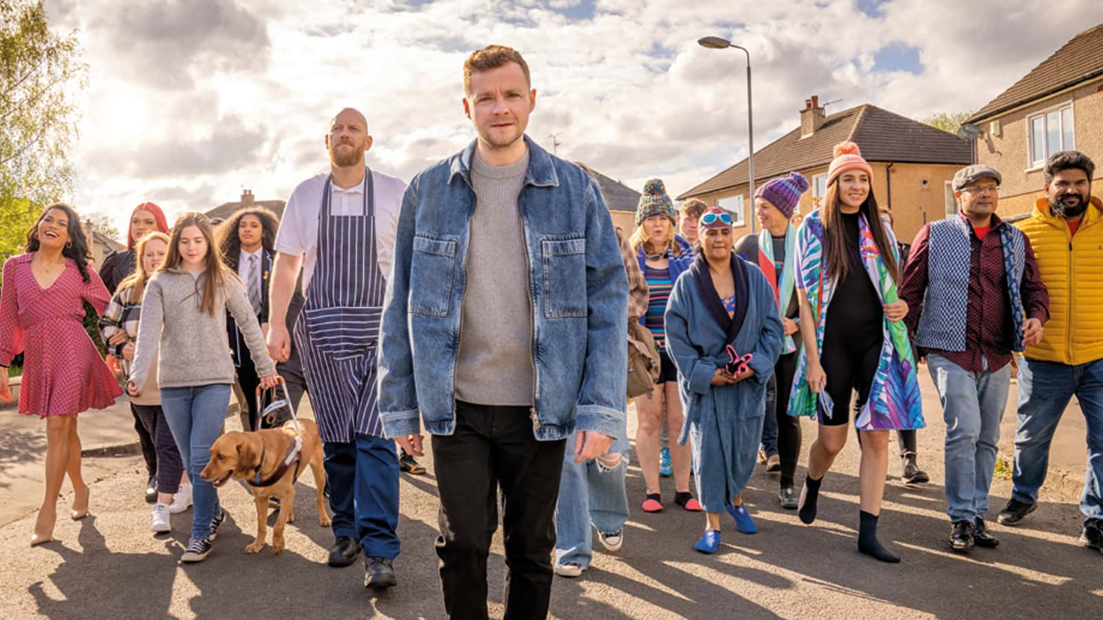 Man walking smiling, with a large group of random people following him on the street