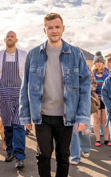 Man walking smiling, with a large group of random people following him on the street