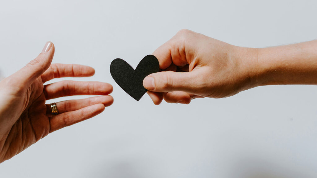 Hand holding out a black heart shape to another hand