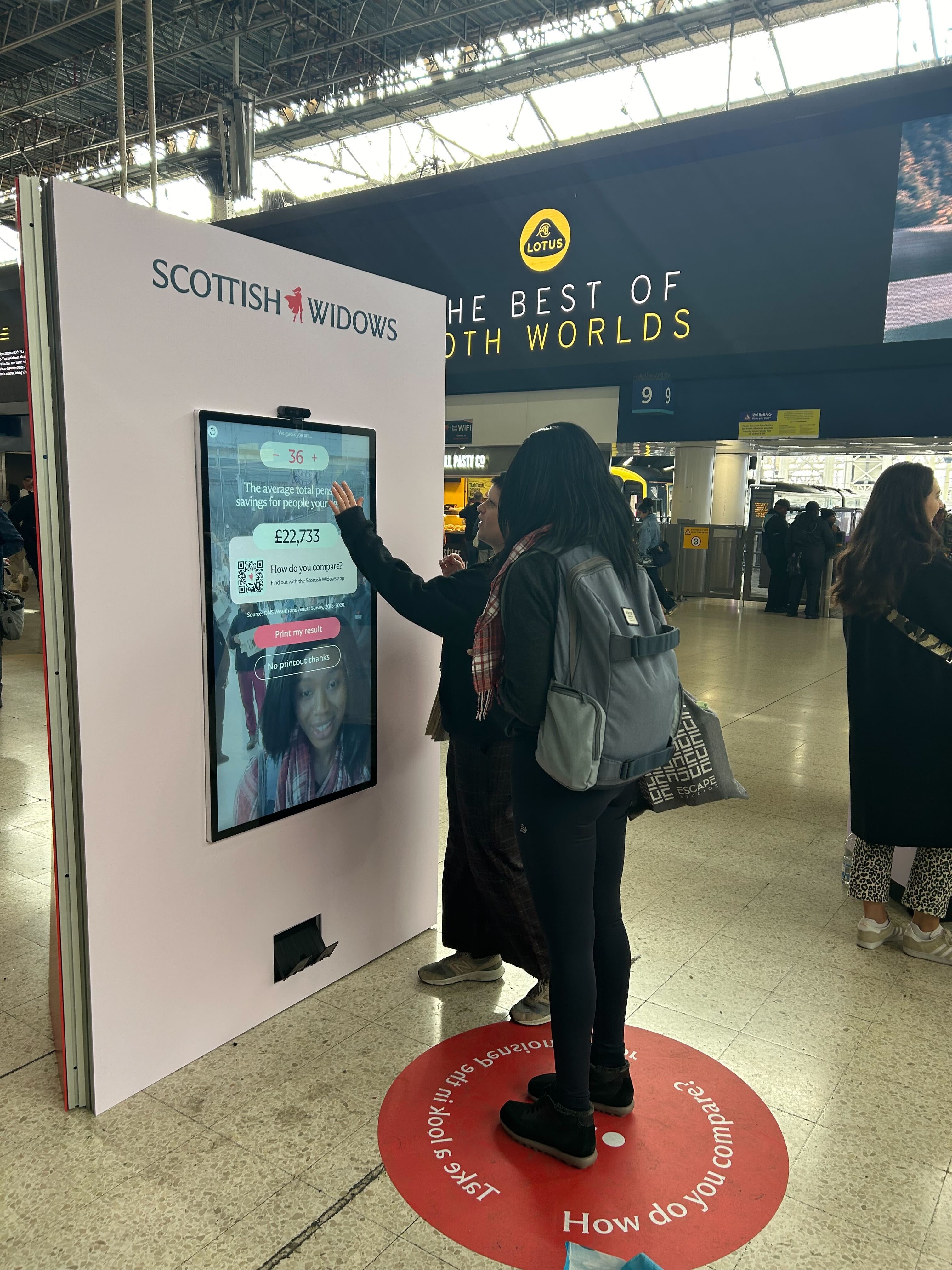 Two women using digital display screen in train station